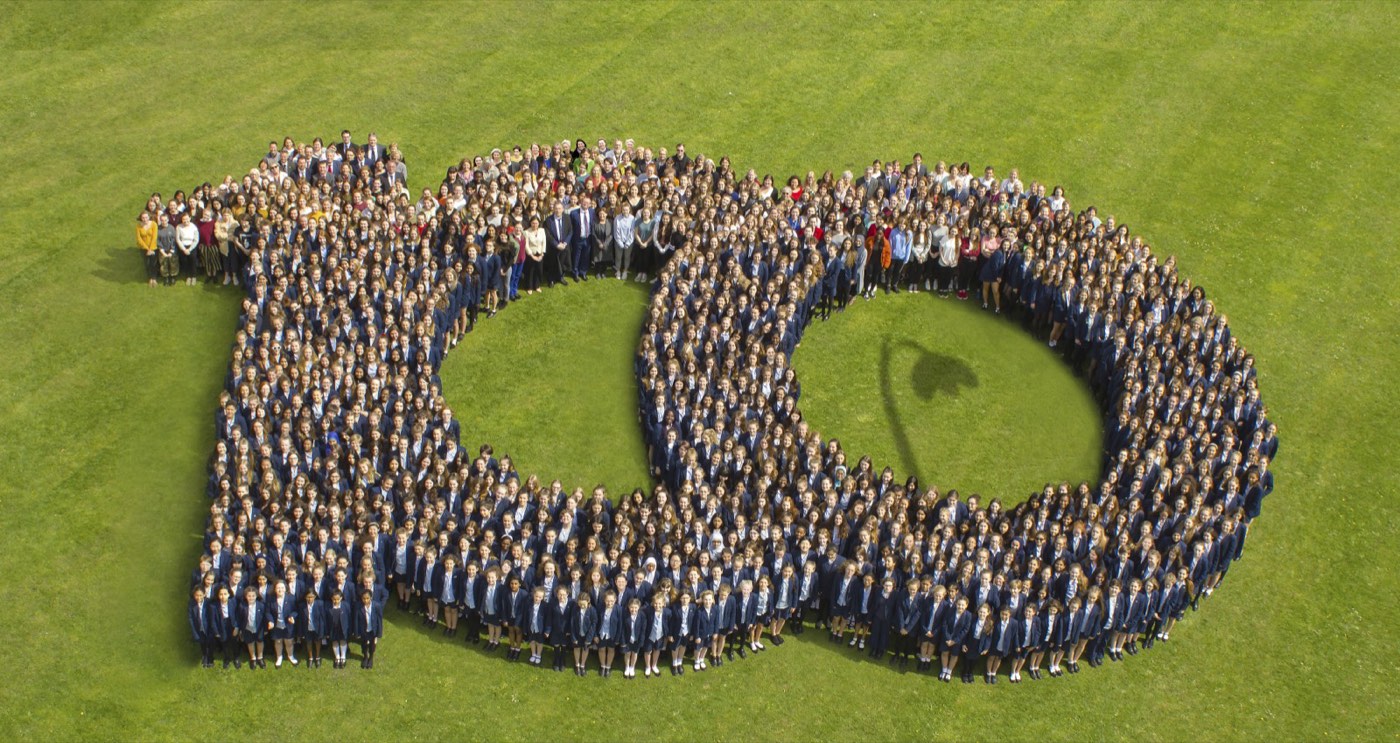 Students and staff arranged on the school field to form the number one hundred for an anniversary photograph